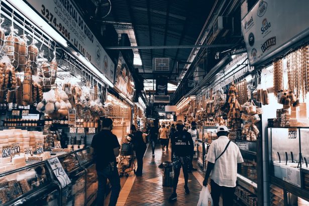 Corredor de mercado interno movimentado, com lojas, pessoas circulando e consumidores fazendo compras.