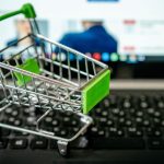 Carrinho de compras em miniatura sobre o teclado de um laptop, simbolizando compras pela internet.
