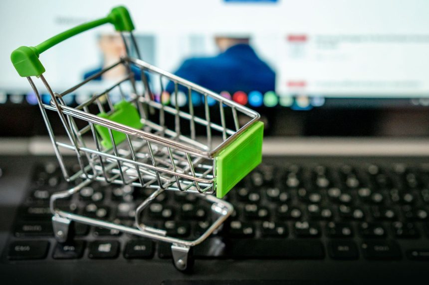 Carrinho de compras em miniatura sobre o teclado de um laptop, simbolizando compras pela internet.