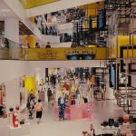 Shopping movimentado, com consumidores circulando entre lojas de varejo em um ambiente contemporâneo.