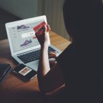 Mulher faz compras online usando um laptop e um cartão de crédito sobre uma mesa.