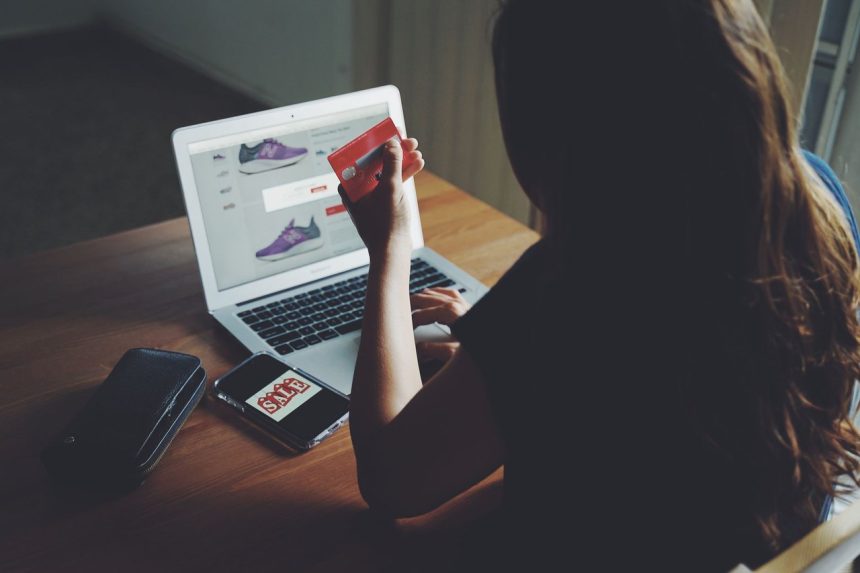Mulher faz compras online usando um laptop e um cartão de crédito sobre uma mesa.